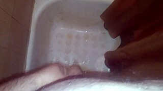 A guy jerks off while peeing and shoots his jizz everywhere.